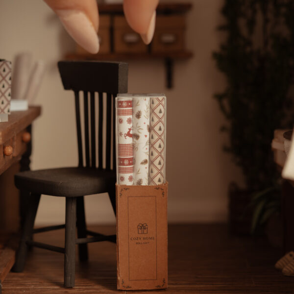 Rollos de papel de regalo en miniatura con estampados navideños dentro de una caja rectangular de cartón.