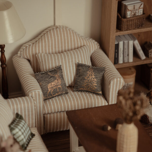 Cojín con un árbol de navidad y otro con un ciervo estampado en dorado brillante. Tela grisácea.