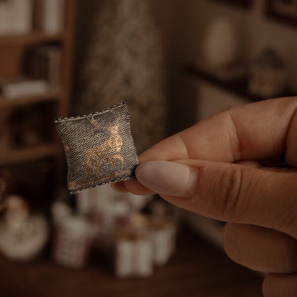 Cojín con un ciervo de navidad estampado en dorado brillante. Tela grisácea.