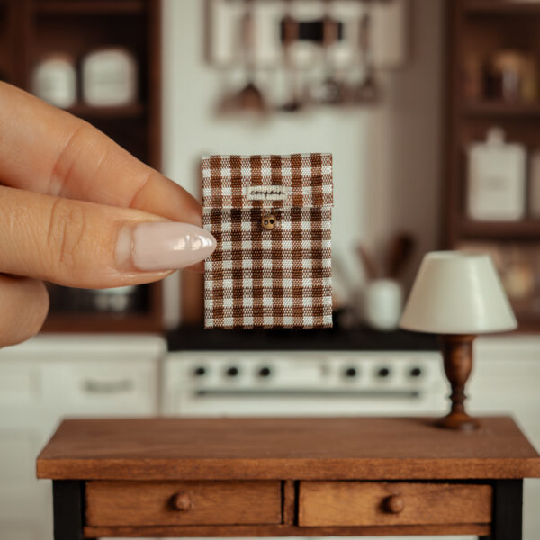 Funda de tela en miniatura con un estampado de cuadros marrones y blancos. Tiene un pequeño broche.